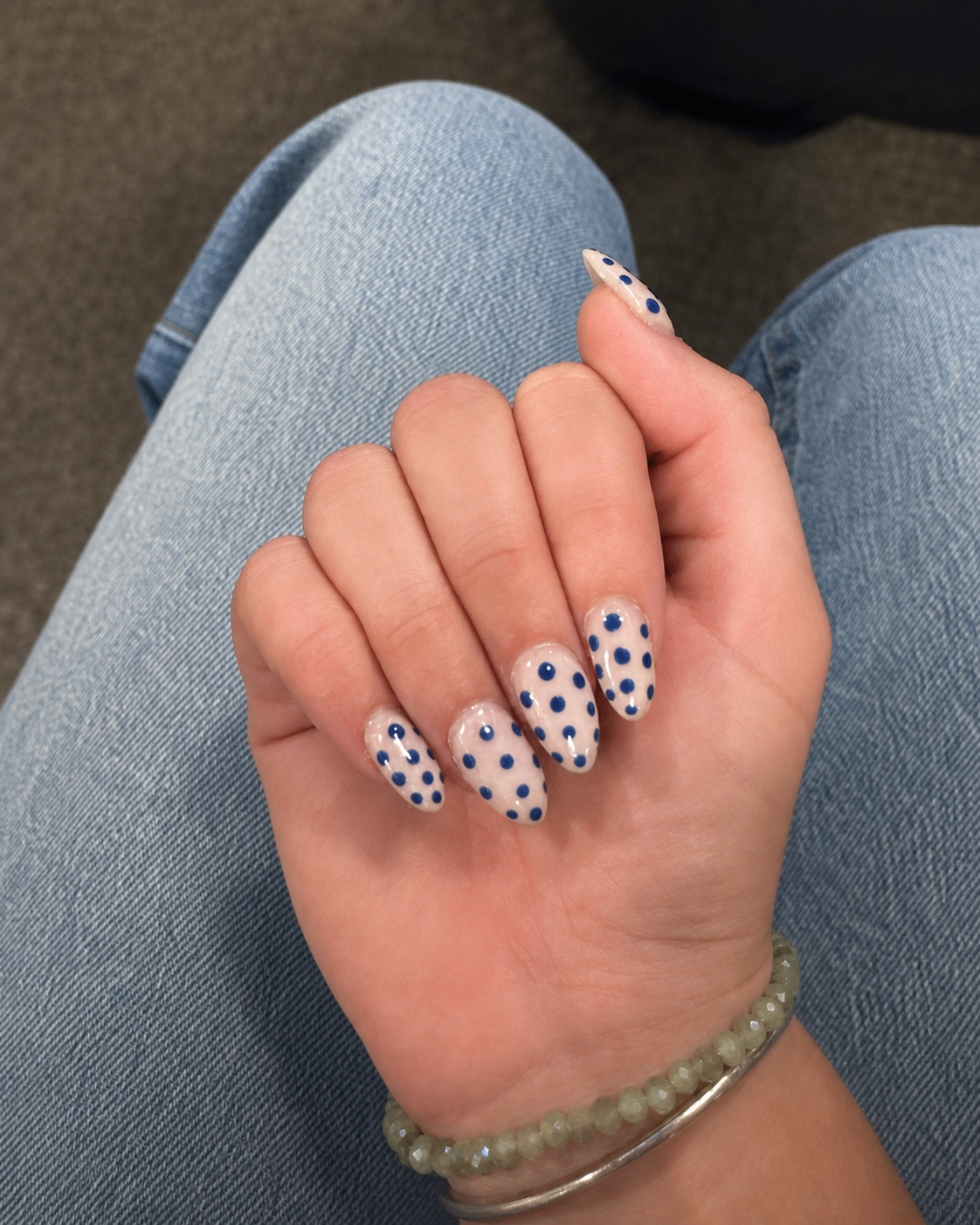 Almond-shaped neutral nails painted with glossy navy-blue polka dots