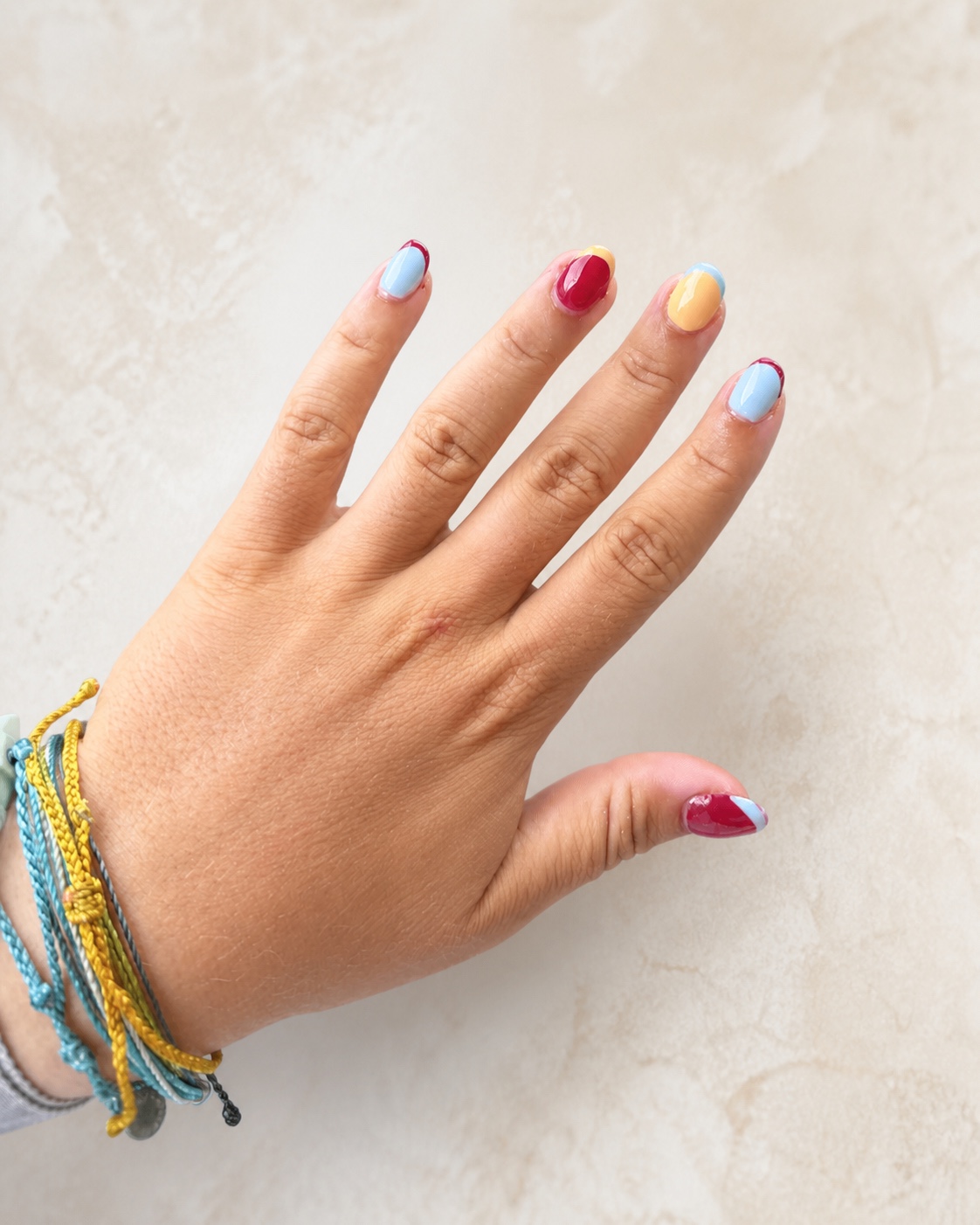 Short rounded nails in light blue, cherry red, and butter yellow color-block designs