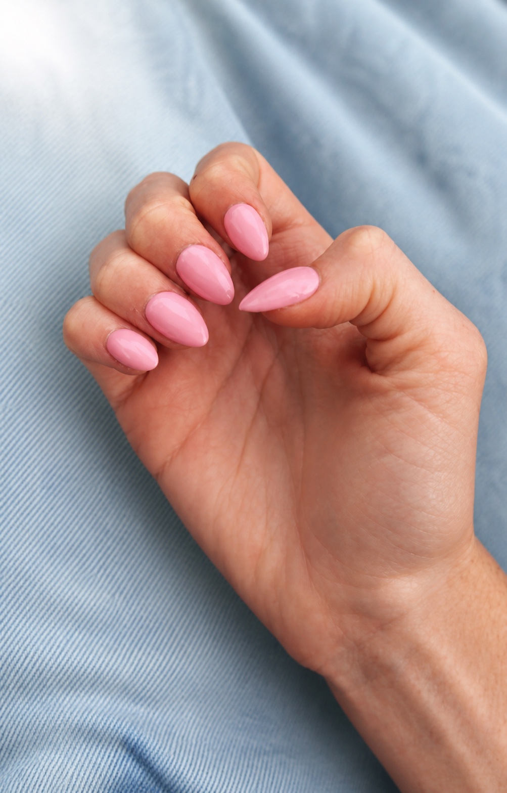 Glossy solid pink almond nails resting against soft light denim